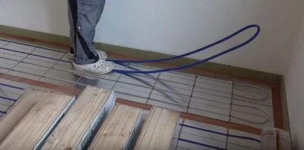 Instalace podlahového vytápění s trubkami pomocí dřevěných lišt a dlažby.