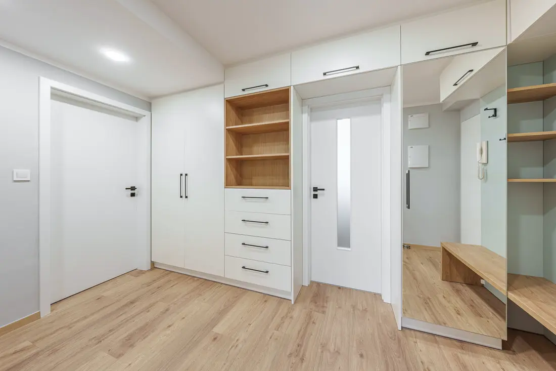 Modern interiér s bílými skříněmi a dveřmi do bytu.