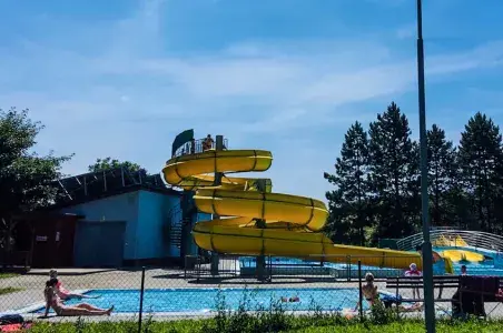 Žluté vodní skluzavky v bazénu s lidmi na lehátkách.