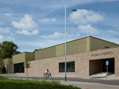 Exteriér bazénu Aquav Parku v Kyjově s cyklisty u budovy.