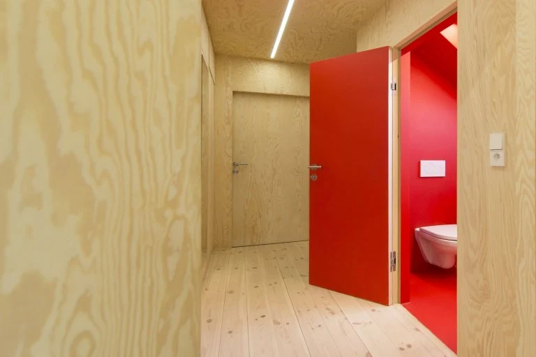Moderní dřevěná chodba s červenými dveřmi do koupelny.