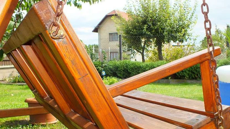 Hnědá dřevěná houpačka na zahradu visící na řetězích.