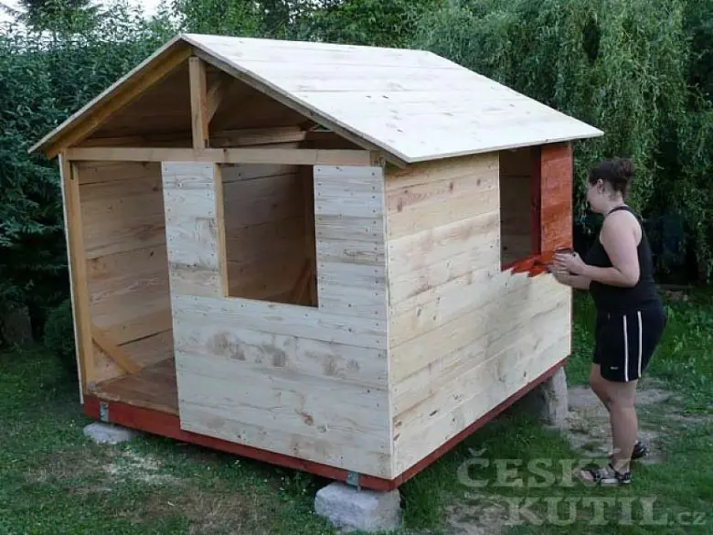 Žena montuje dřevěné panely na dětský zahradní domek.
