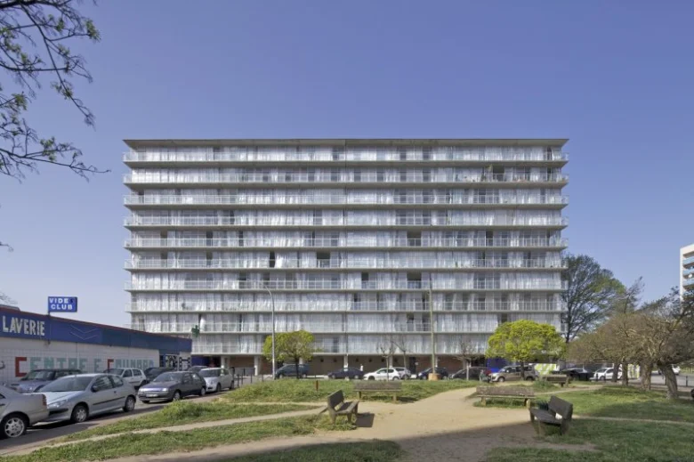 Velká betonová budova panelového domu s balkony pod modrou oblohou.