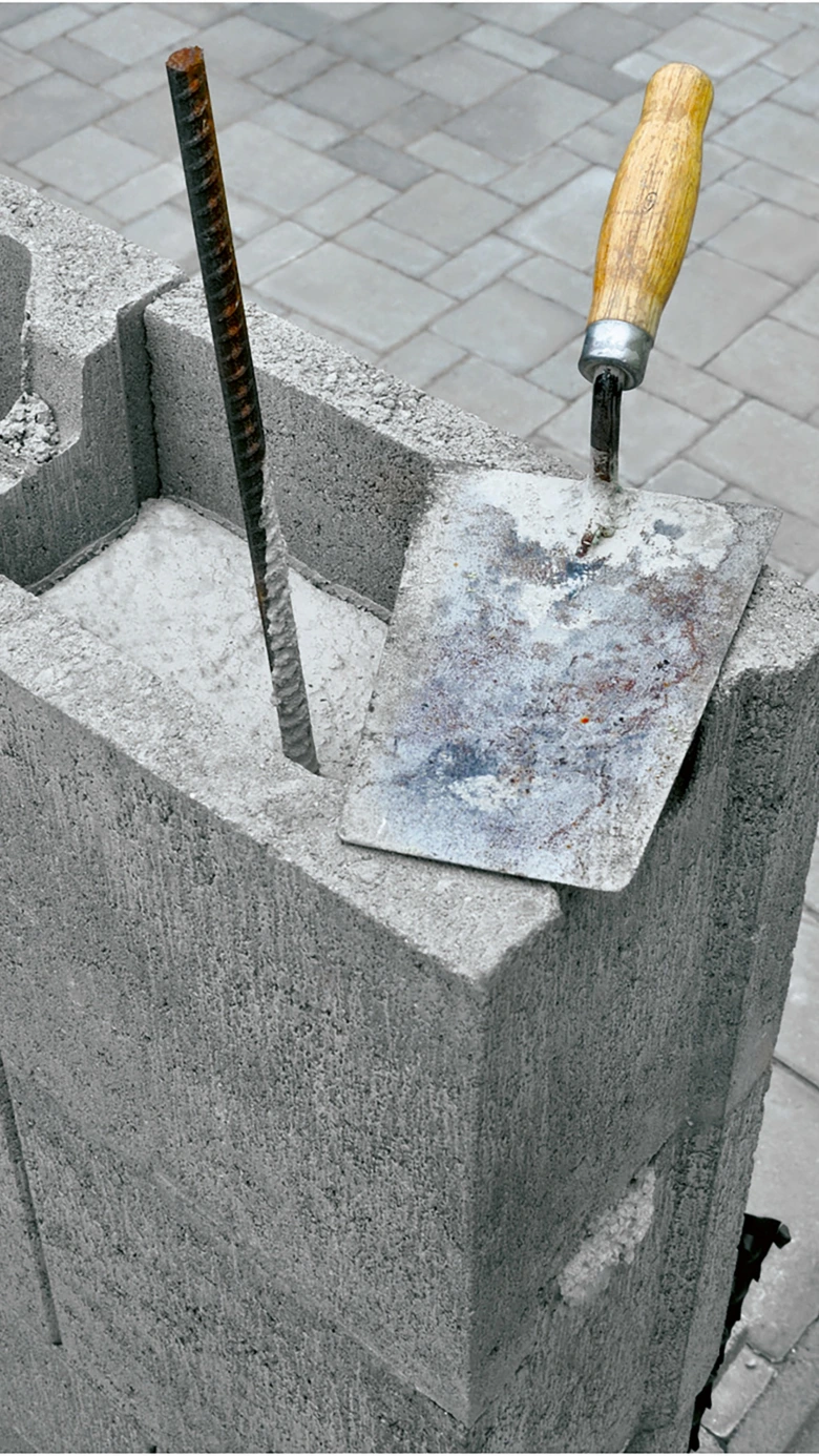 Betonový cihlový blok s výztuží a kladivem na stavebním objektu.