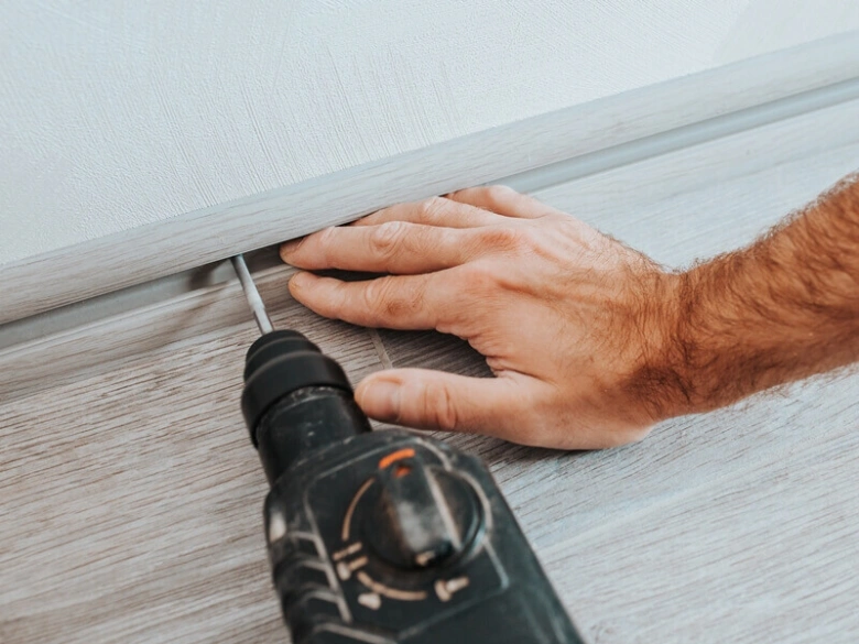 Muž vrtá do podlahy při pokládce linolea nebo laminátu.